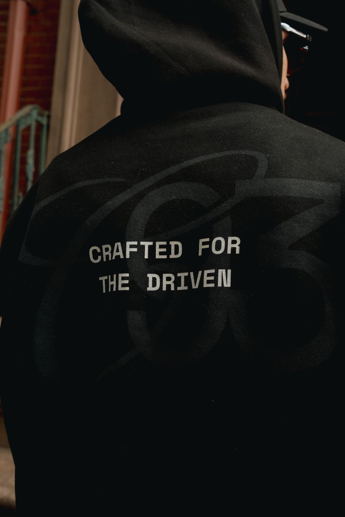 A person wearing a black hoodie, shown from the back, with the text 'CRAFTED FOR THE DRIVEN' printed in white across the upper back.